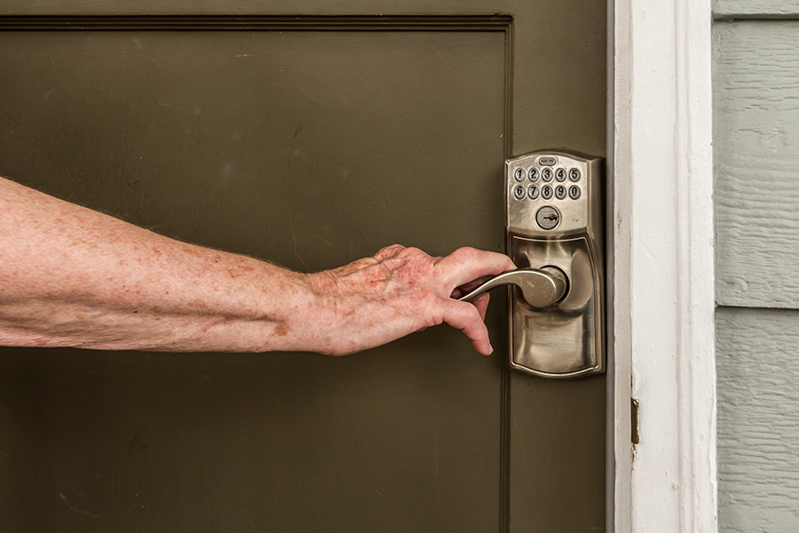 A woman's hand grips the lever-style handle on the greenish-brown front door of the home.